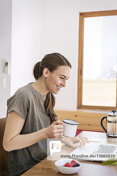 Happy woman using laptop while sitting at table in home