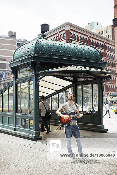 Man playing guitar while standing on street in city