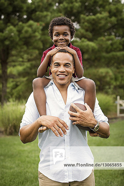 Portrait of father and son with football ball standing in backyard