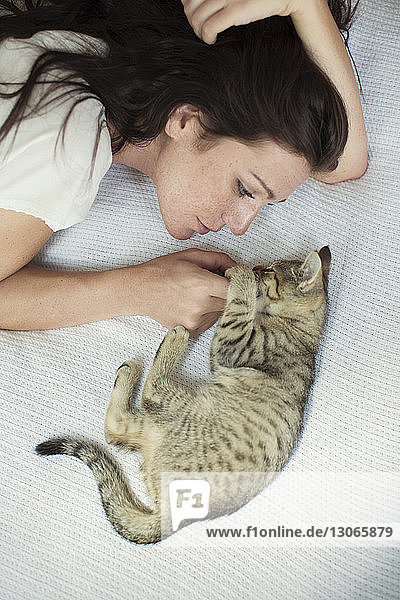 Hochwinkelansicht einer Frau mit Katze  die zu Hause auf dem Bett liegt
