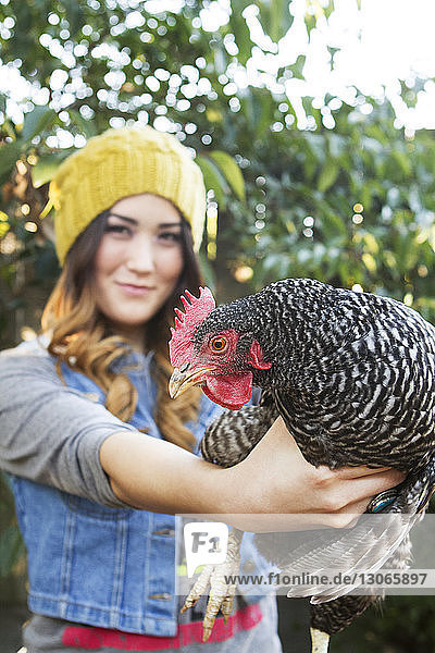 Porträt einer glücklichen Frau  die eine Henne auf dem Bauernhof hält