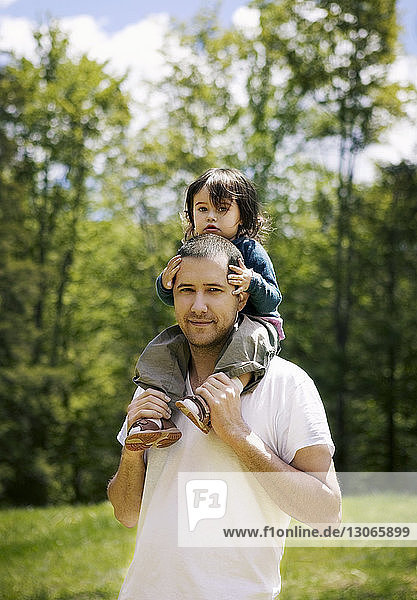Portrait of man carrying girl on shoulder while standing in field