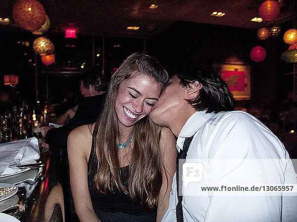 Man kissing smiling girlfriend in restaurant