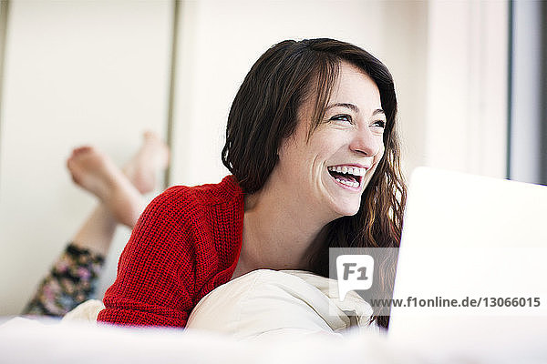 Cheerful woman with laptop computer lying on bed at home