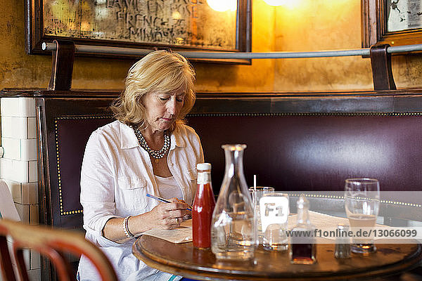 Frau hält Stift  während sie am Tisch im Restaurant sitzt