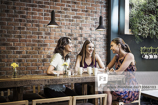 Happy friends having coffee at table by brick wall in cafe