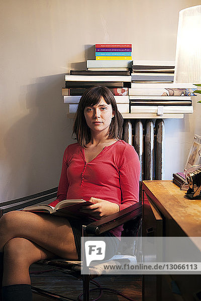 Porträt einer Frau mit Buch  die zu Hause auf einem Stuhl sitzt