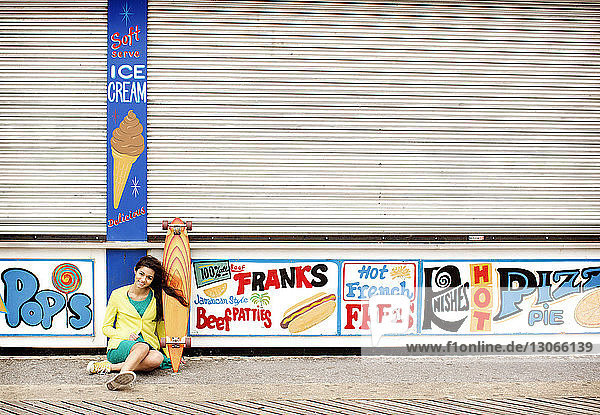 Porträt eines Teenagers mit Skateboard vor geschlossenen Lebensmittelgeschäften sitzend