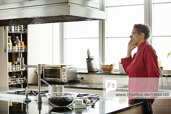 Seitenansicht einer Frau  die mit einem Smartphone spricht  während sie in der Küche steht