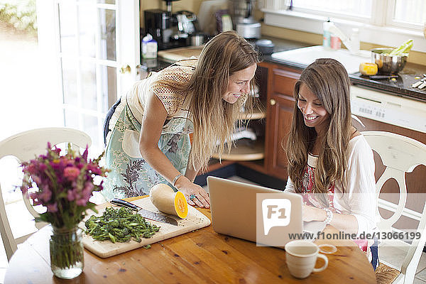 Glückliche Frauen  die einen Laptop-Computer benutzen  während sie zu Hause Essen zubereiten