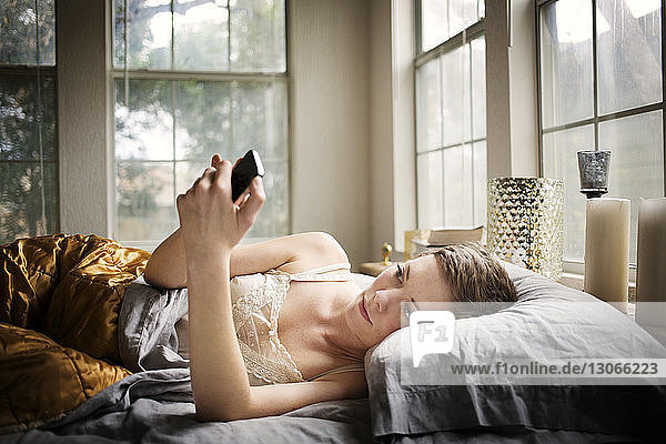 Frau benutzt Smartphone  während sie zu Hause im Bett liegt