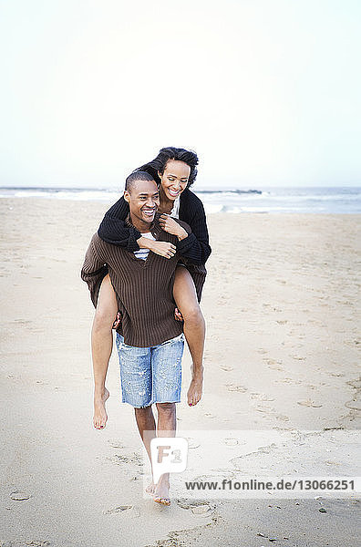 Mann nimmt seine Freundin huckepack  während er am Strand auf Sand läuft