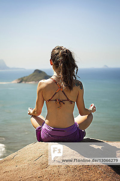 Rear view of woman meditating while sitting on rock