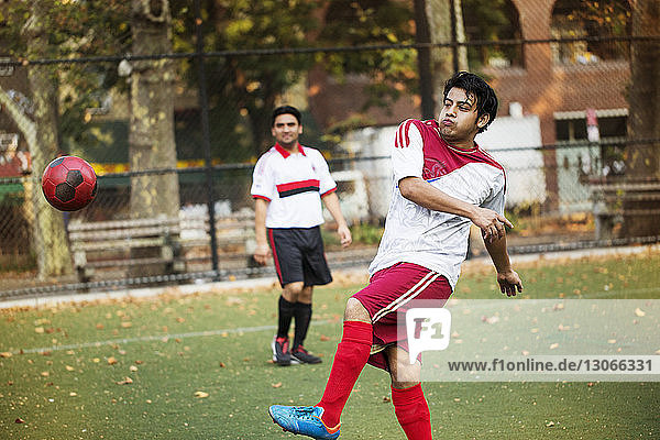 Fußballspieler kickt Ball  während ein Freund auf das Feld schaut