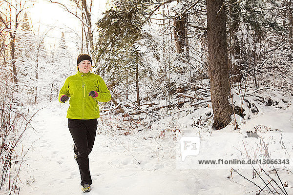 Frau rennt an Bäumen vorbei auf schneebedecktem Feld im Wald