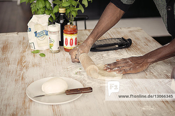 Midsection of man rolling dough at kitchen table