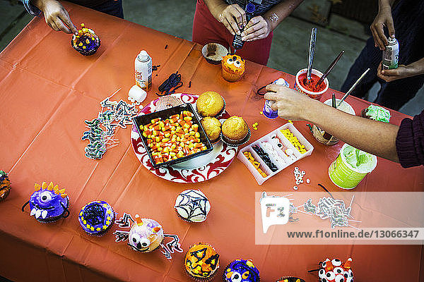 Mutter und Kinder dekorieren Muffins am Tisch während der Halloween-Party