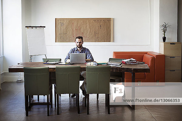 Mann benutzt Laptop-Computer  während er im Büro am Schreibtisch sitzt