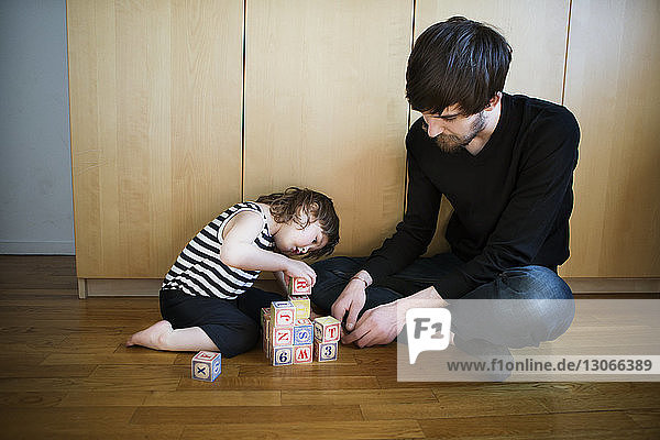 Vater sieht Tochter beim Spielen mit Spielzeugblöcken an  während er auf dem Boden sitzt