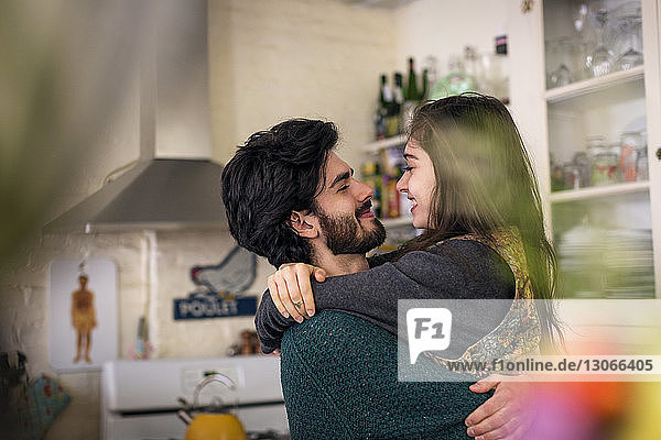 Happy couple embracing while standing at kitchen