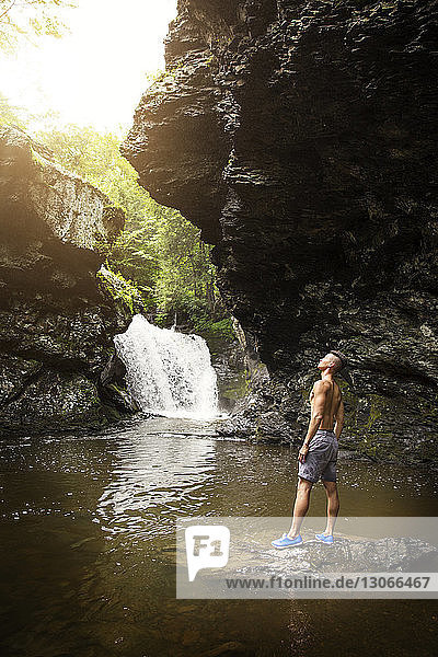 Mann schaut auf  während er auf einem Felsen im See steht