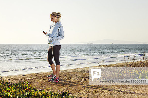 Seitenansicht einer Frau  die ein Smartphone benutzt  während sie am Strand am Ufer steht