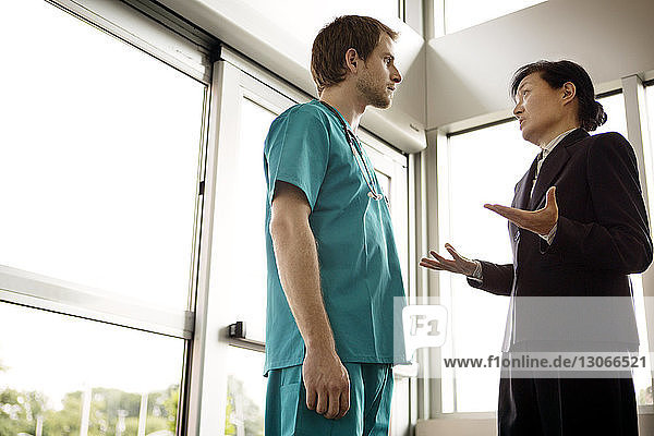 Low angle view of doctor talking with businesswoman while standing in hospital