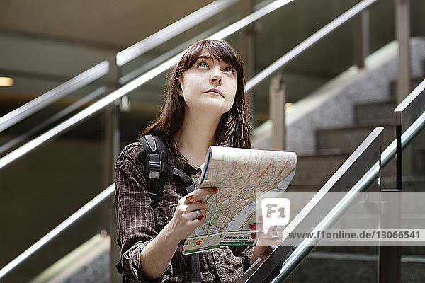 Frau mit Reiseführer schaut auf  während sie auf der Treppe am Bahnhof steht