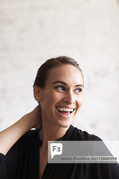 Cheerful woman looking away while standing against wall