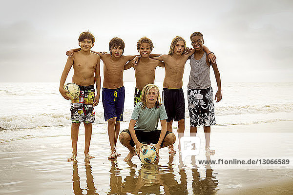 Portrait of friends with soccer ball on shore at beach