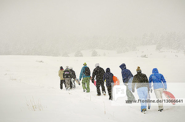 Rear view of people carrying sled while walking on snow covered field