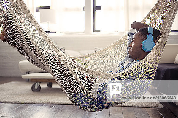 Man listening music while resting on hammock in living room at home