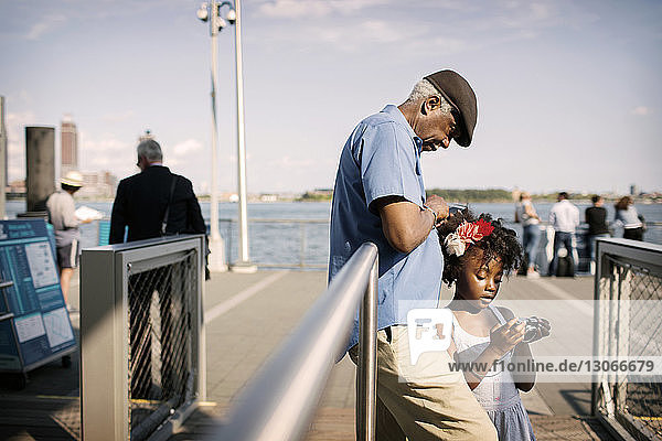 Großvater und Enkelin schauen in die Kamera  während sie auf der Promenade am Geländer stehen