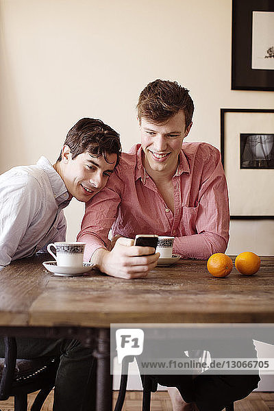 Schwules Paar benutzt Smartphone  während es zu Hause am Tisch sitzt