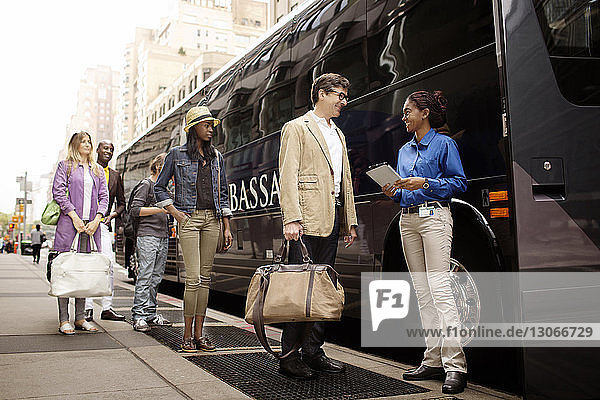 Fröhlicher Reiseführer schaut Touristen an  während er auf der Straße gegen den Bus steht