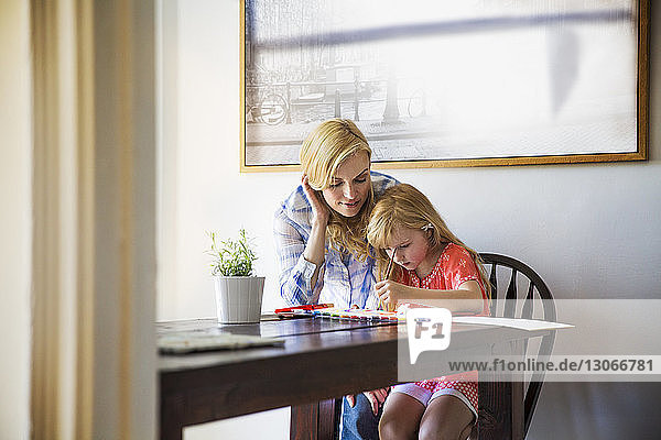 Mother looking at girl painting while sitting at table