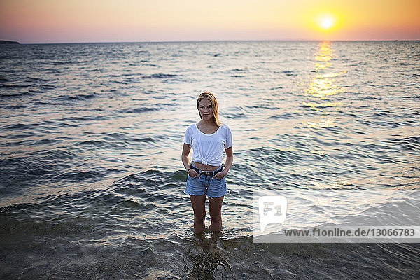 Portrait of woman with hands in pockets standing in water at beach