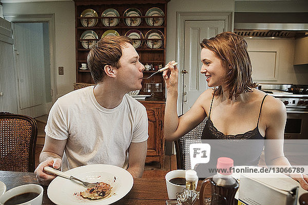 Woman feeding man while sitting at dining table in home