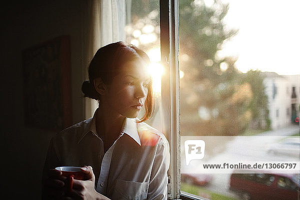 Woman looking away while sitting by window at home