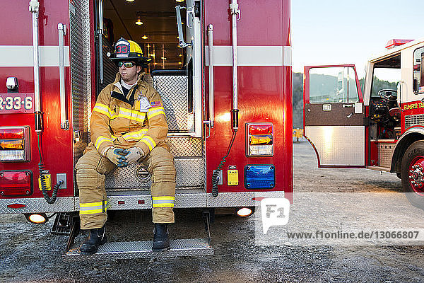 Feuerwehrmann schaut weg  während er auf den Stufen eines Feuerwehrwagens sitzt