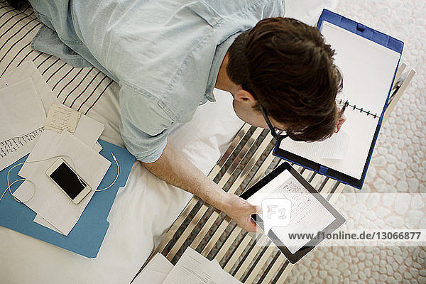 Overhead view of man using tablet computer while working on bed at home