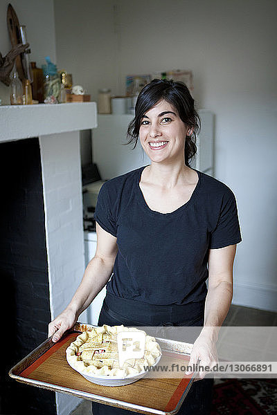 Porträt einer Frau  die zu Hause stehend ein Tablett mit Kuchen hält