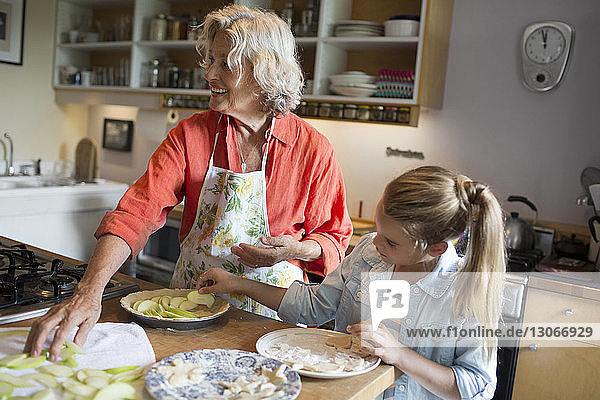 Frau mit Enkelin beim Anrichten von Apfelscheiben im Teller
