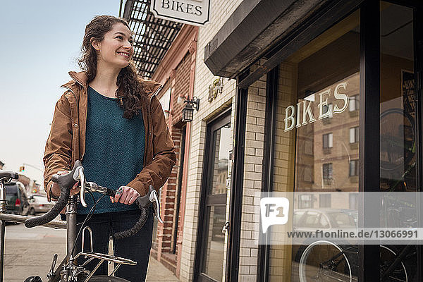 Smiling woman looking away while standing on footpath against bicycle shop