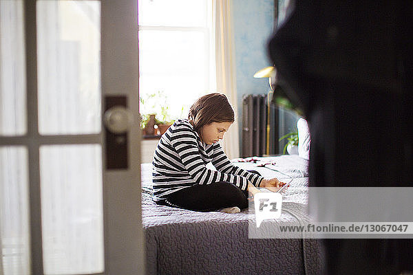 Mädchen benutzt Tablet-Computer  während sie auf dem Bett sitzt und durch die Tür gesehen wird