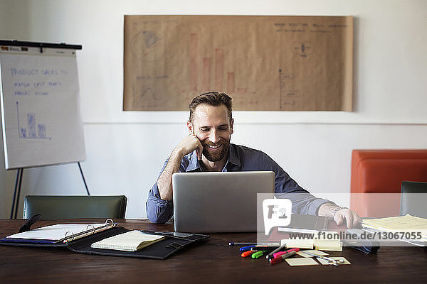 Lächelnder Geschäftsmann schaut auf Laptop-Computer  während er im Büro sitzt
