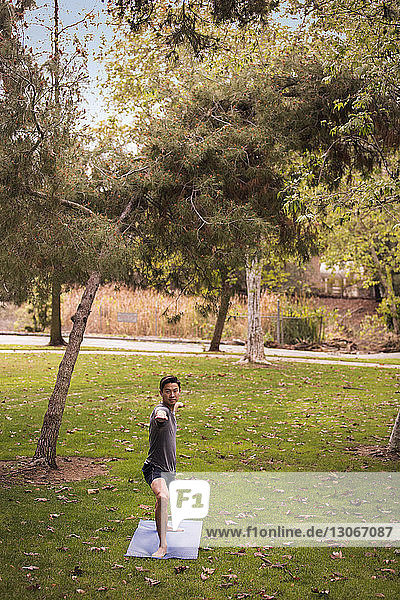 Sportler übt Kriegerpose auf Übungsmatte im Park