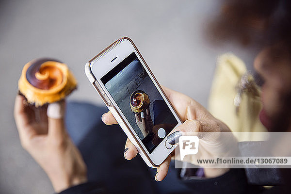 Ausgeschnittenes Bild einer Frau  die mit einem Smartphone Muffin fotografiert