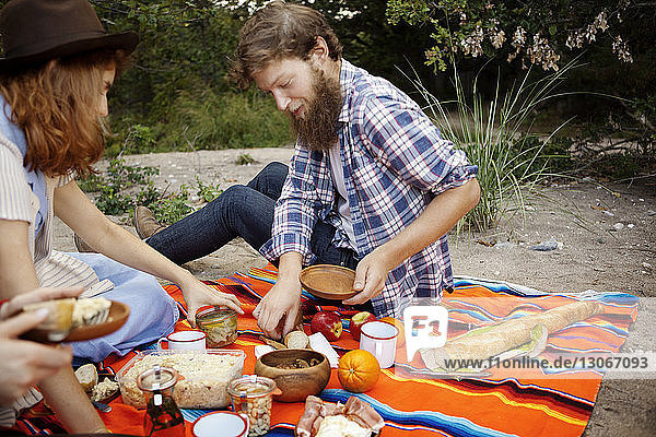Freunde beim Frühstück auf einer Picknickdecke im Wald sitzend