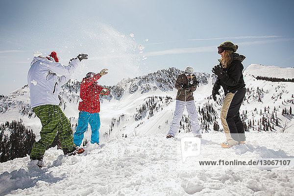 Glückliche Skifahrer spielen mit Schnee  während sie auf einem schneebedeckten Feld stehen